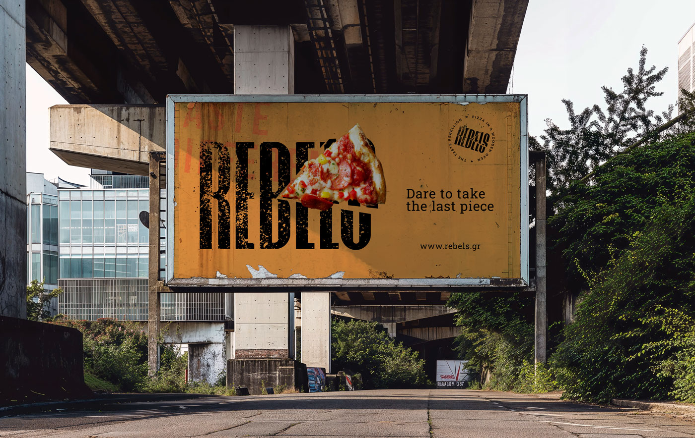 Outdoor billboard advertisement for Rebels Pizza under a concrete overpass. The design features a distressed yellow background, the bold Rebels cut-typography logo, a real pizza slice, and the tagline "Dare to take the last piece."